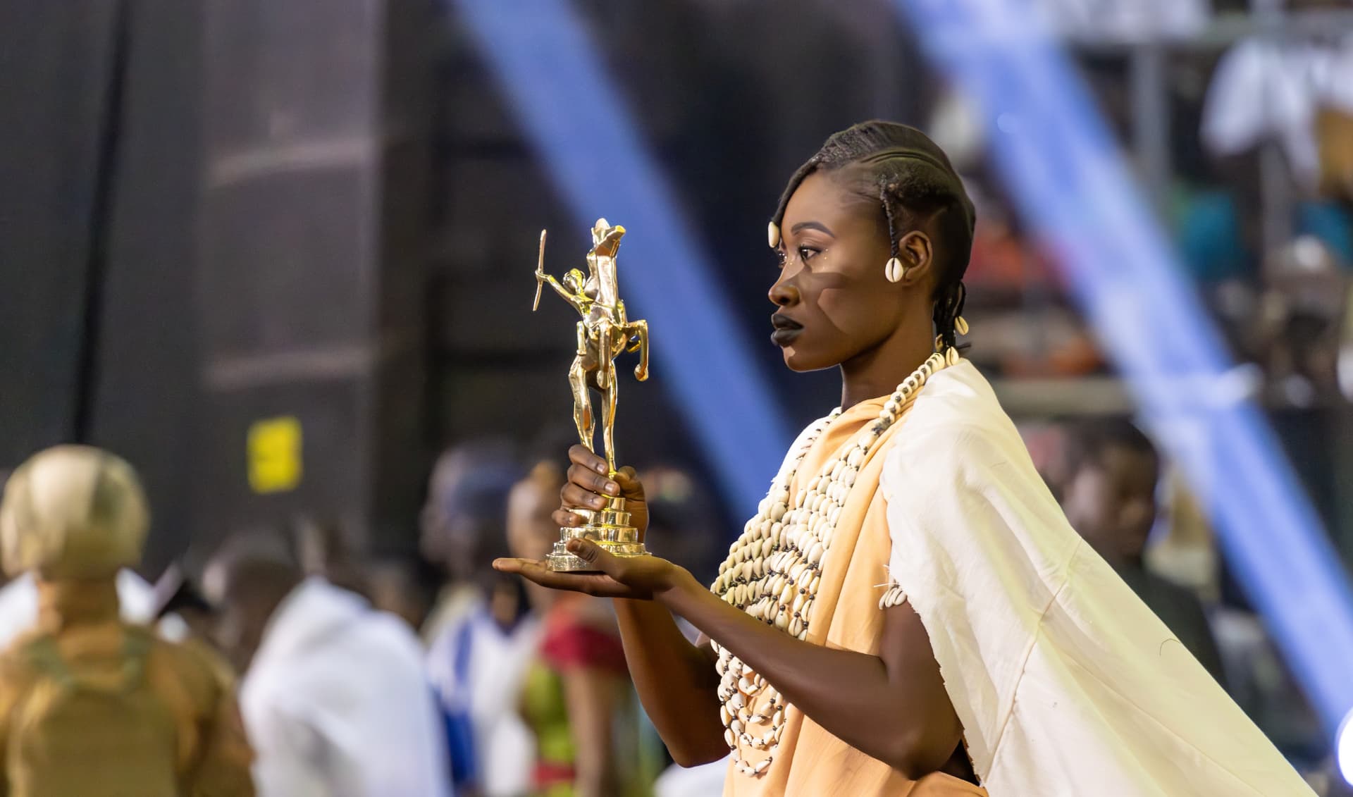 Laureate en tenue traditionnelle presentant son trophee dore sur scene