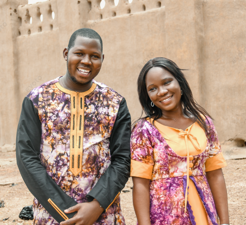 Couple en tenues traditionnelles assorties devant une case en banco